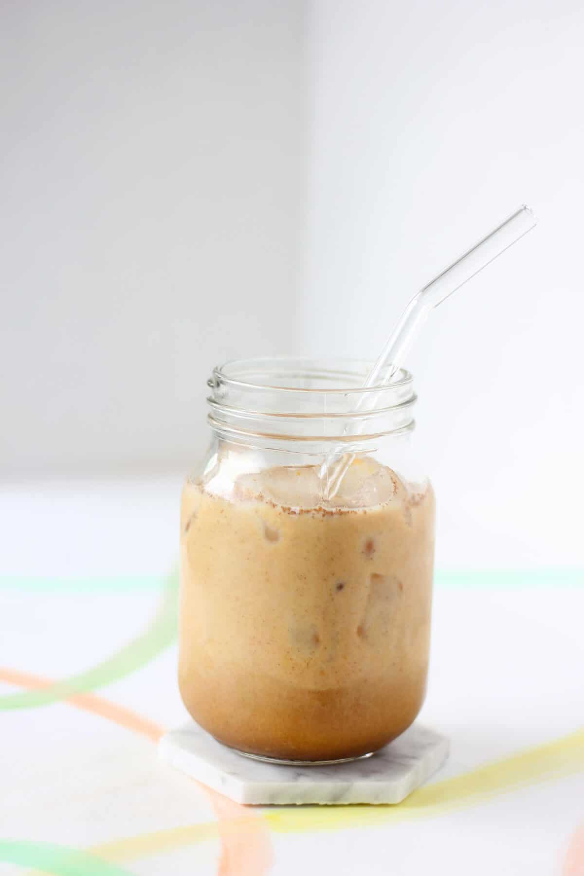 Clear jar filled with ice and creamy coffee with a clear glass straw.