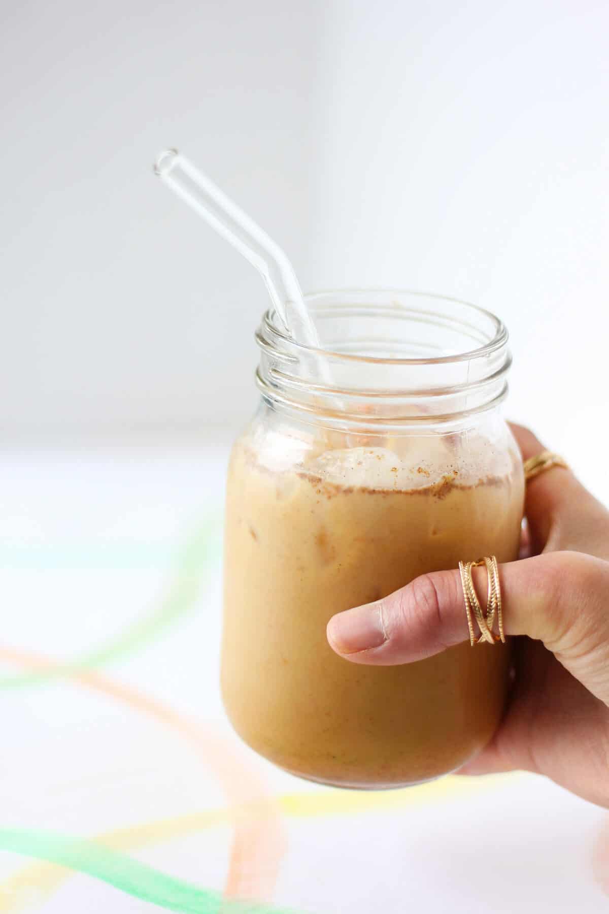 Hand holding a clear jar filled with ice and creamy coffee with a clear glass straw.