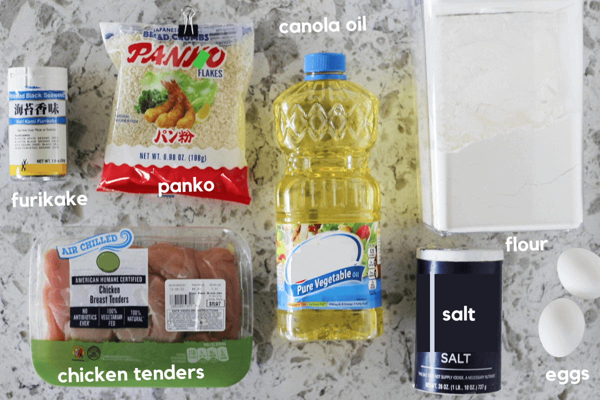 Ingredients for furikake chicken laid on a counter, including furikake, panko, canola oil, flour, eggs, salt and chicken tenders.