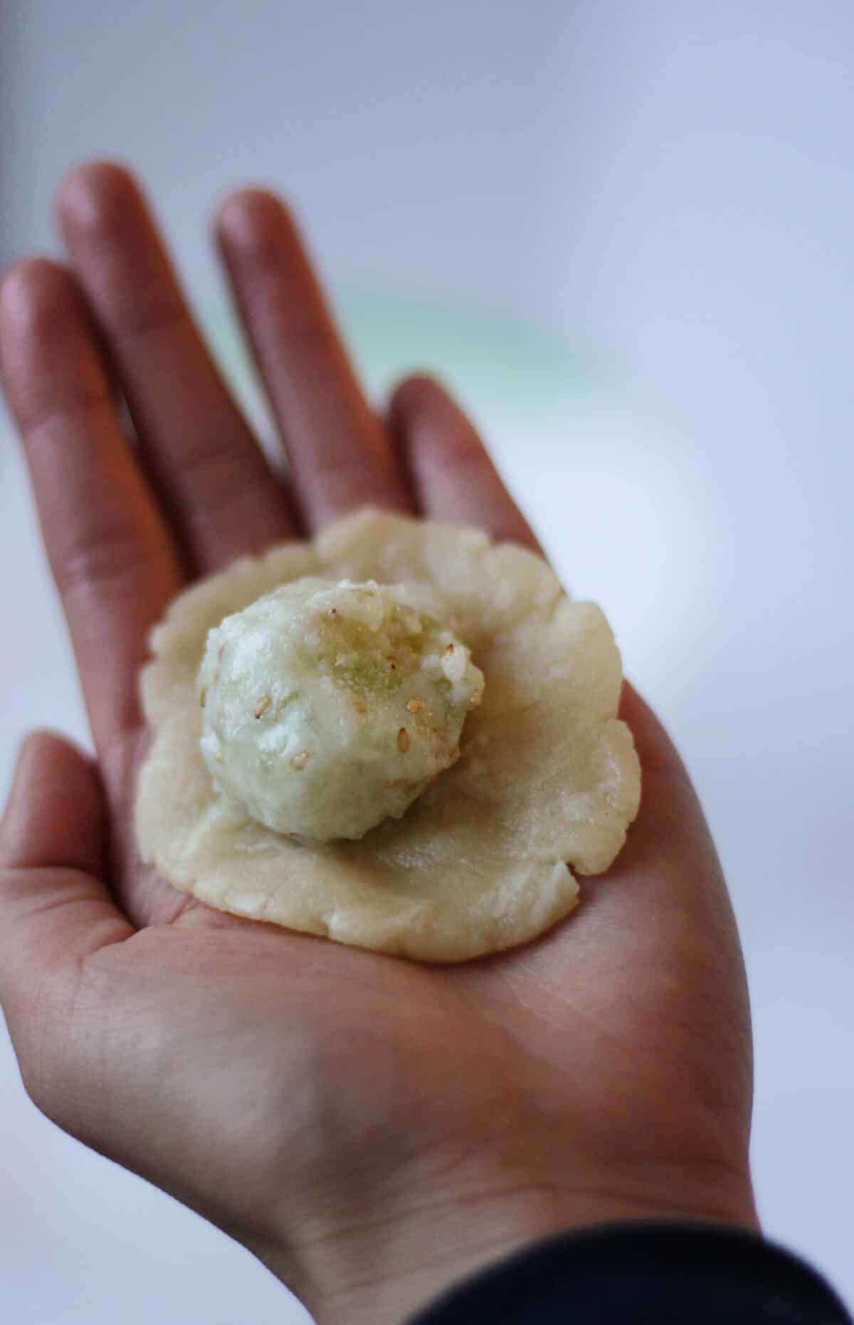 A piece of flattened pastry dough with a ball of wintermelon filling in someone's palm.
